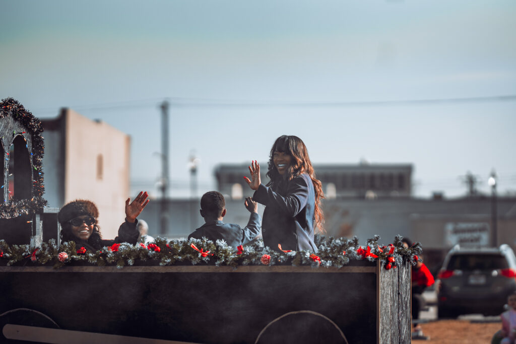 People wave from a festively decorated parade float on a city street