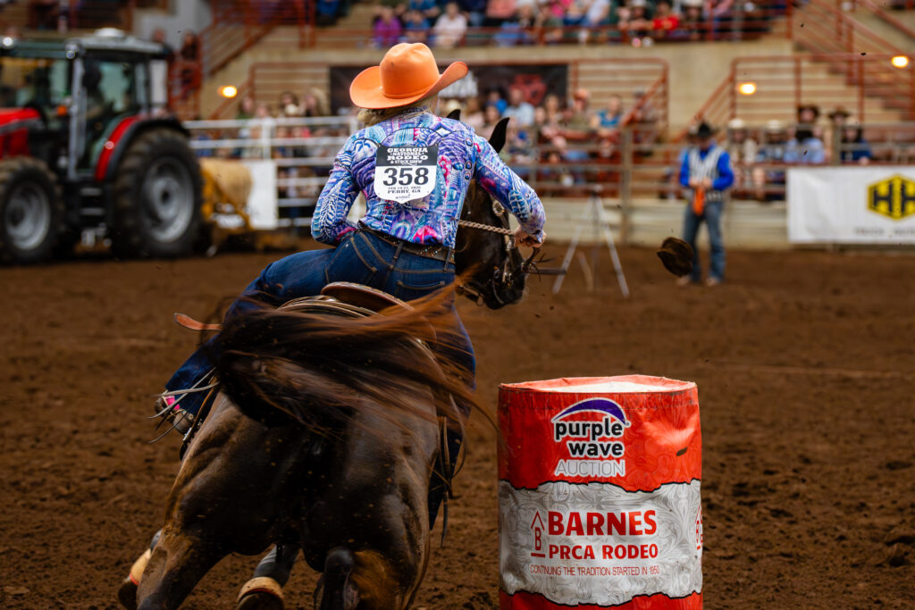 Cowgirl rounding a barrel on horseback during a rodeo barrel race
