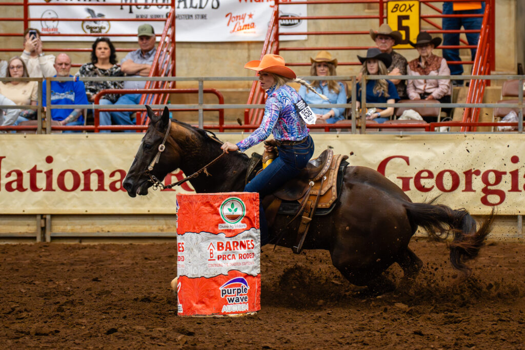 Cowgirl on horseback rounding a barrel at an indoor rodeo event