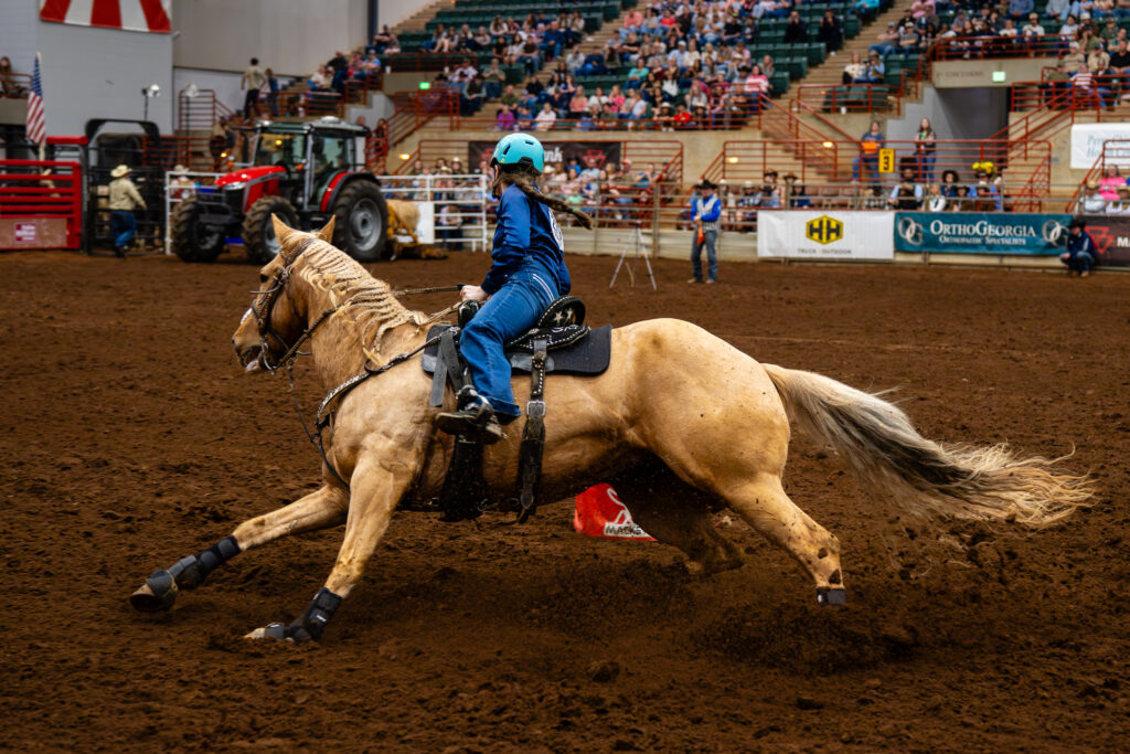 Barrel racer on palomino horse sliding into a sharp turn in an indoor arena