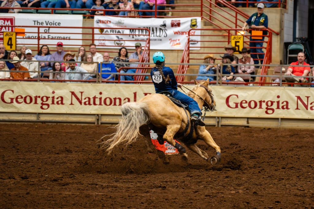 Barrel racer on palomino horse making a sharp turn in indoor arena