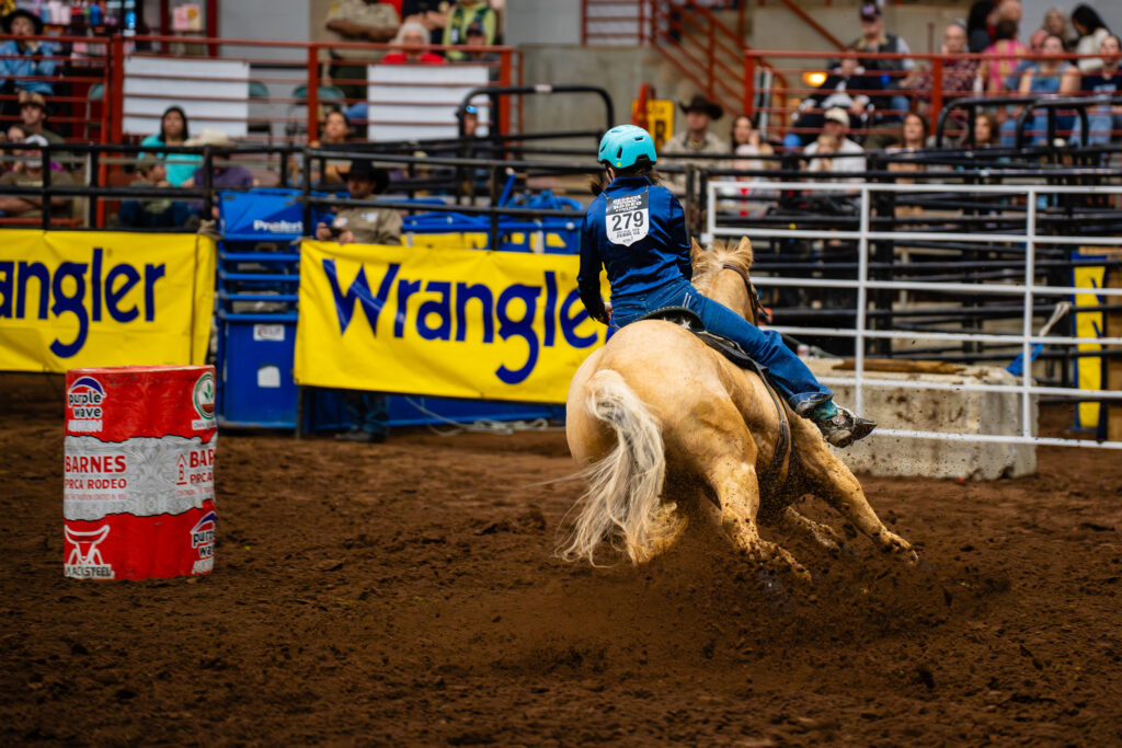 Barrel racer on a palomino horse making a sharp turn around a barrel