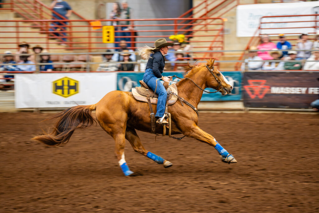 Cowgirl barrel racer galloping on chestnut horse in rodeo arena