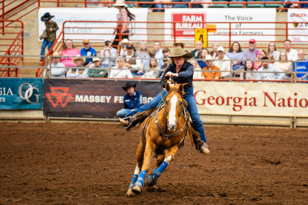 Cowboy on horseback rounding a barrel at an indoor rodeo arena