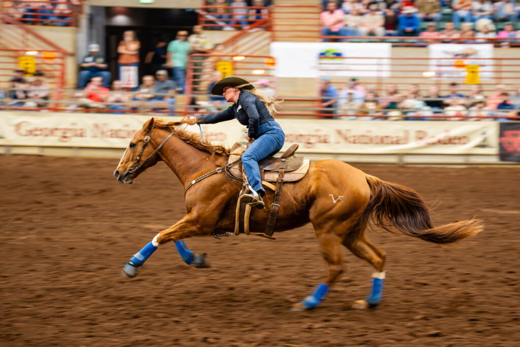 Cowgirl racing a chestnut horse at full speed in an indoor rodeo arena