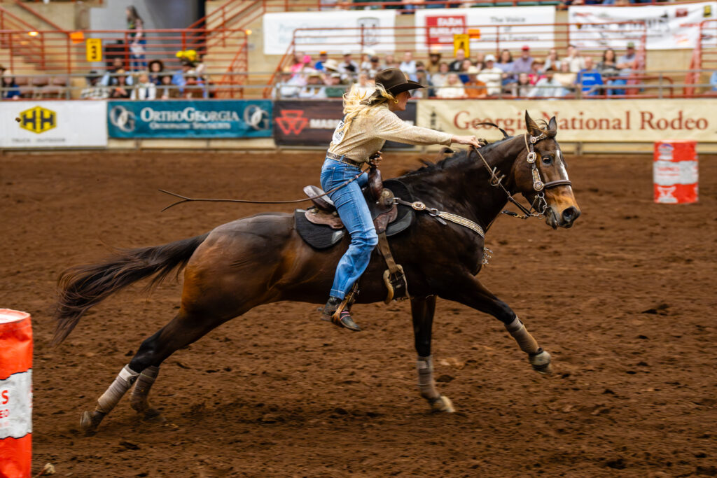 Cowgirl on galloping horse rounding a barrel at a rodeo