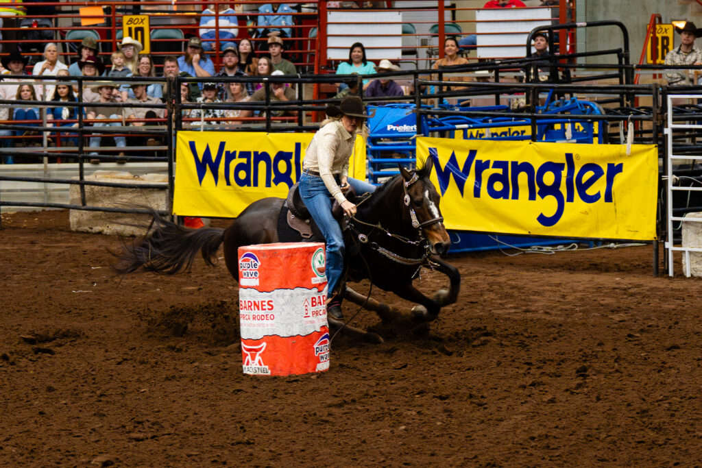 Cowgirl on horseback rounding a barrel during a rodeo barrel racing run