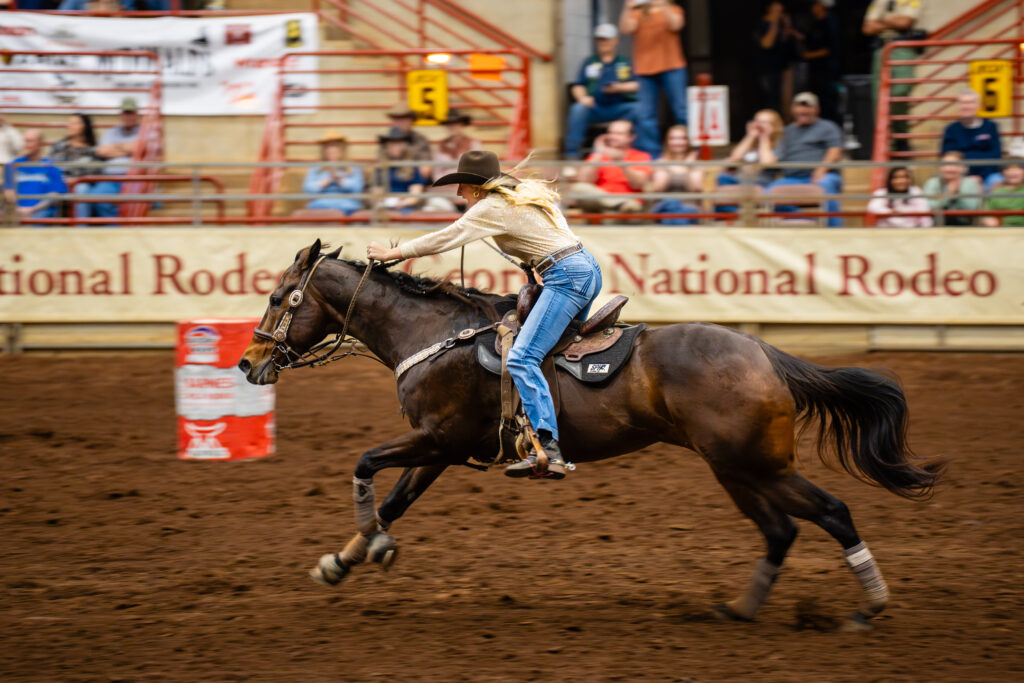 Cowgirl racing her horse past a barrel in an indoor rodeo arena