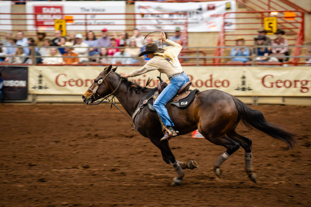 Cowgirl barrel racer riding a galloping horse in a rodeo arena