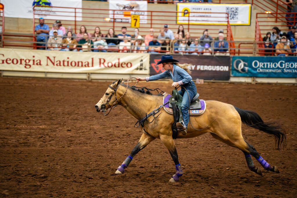 Cowgirl barrel racer galloping on horse at Georgia National Rodeo arena