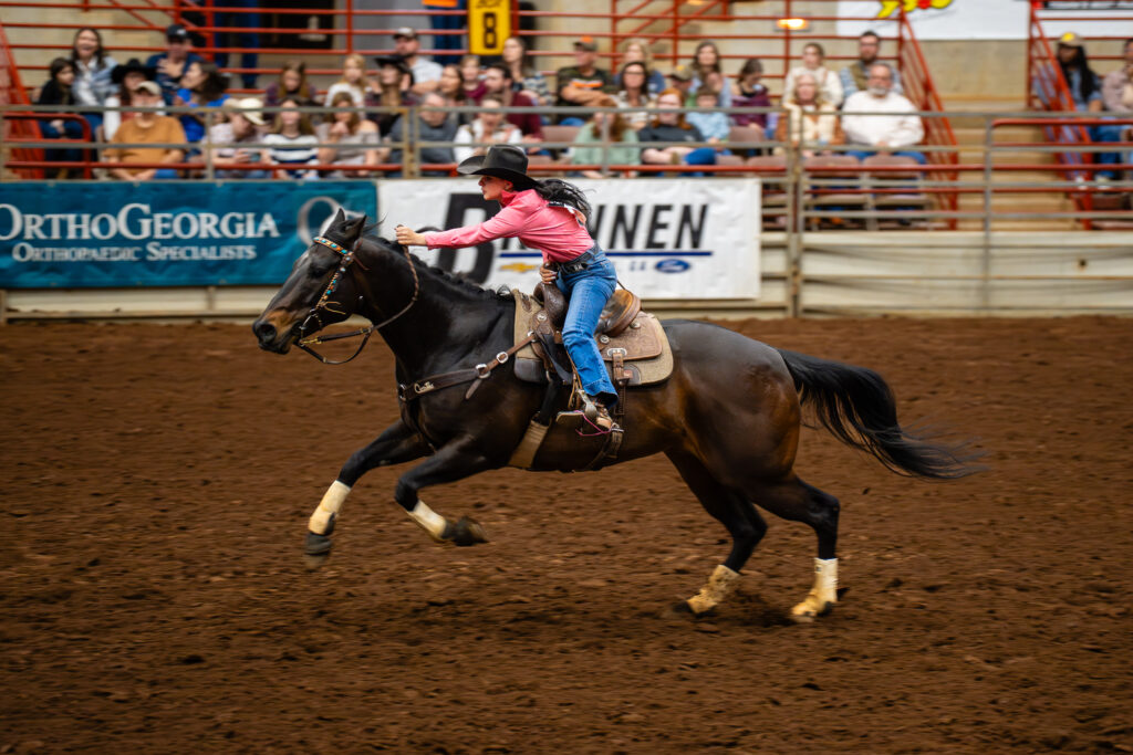 Cowgirl in pink shirt racing a horse across an indoor rodeo arena