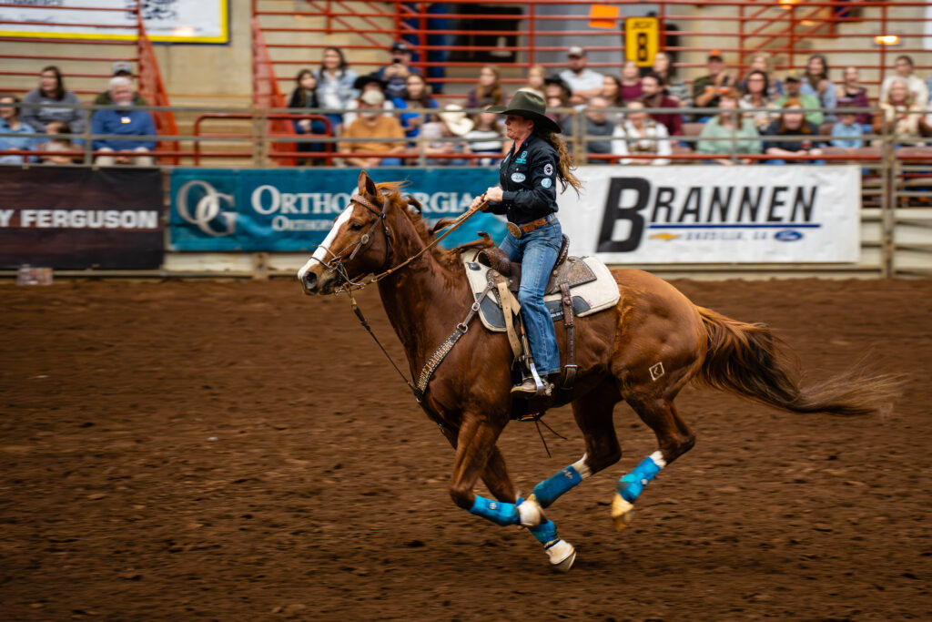 Cowgirl riding a galloping horse in a barrel racing arena