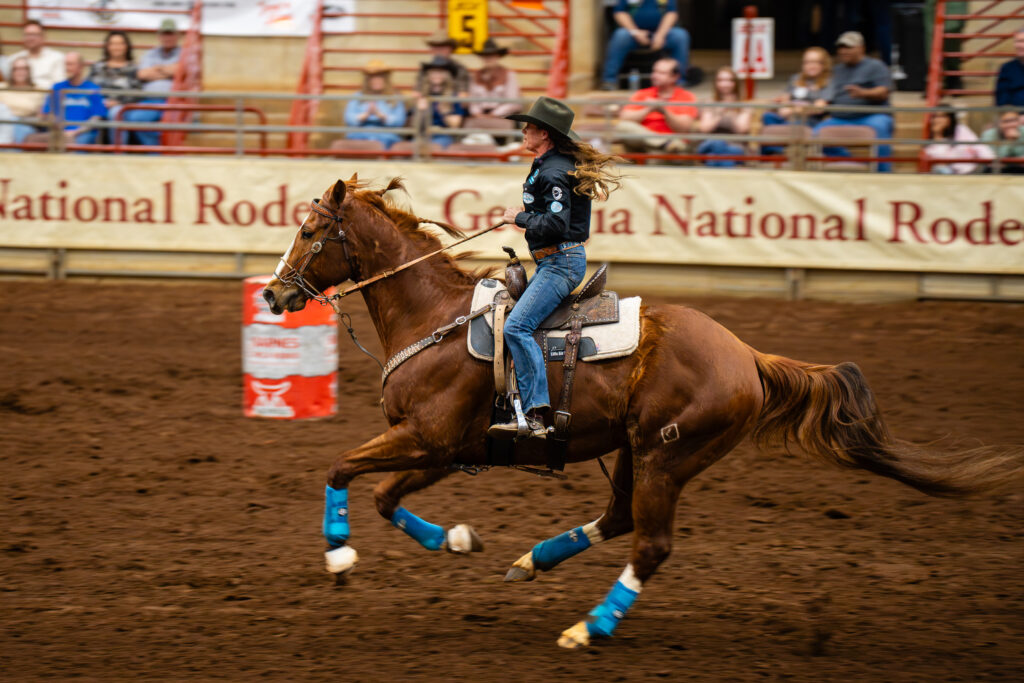 Cowgirl barrel racing on a galloping horse in a rodeo arena