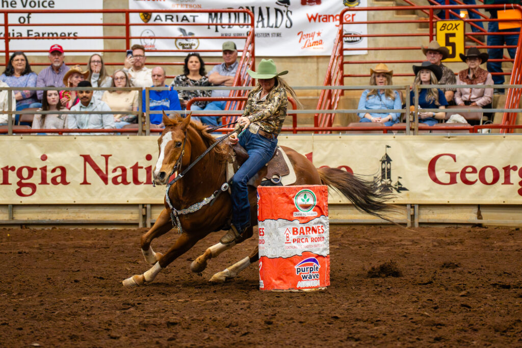 Cowgirl on galloping horse rounding a barrel in a rodeo arena