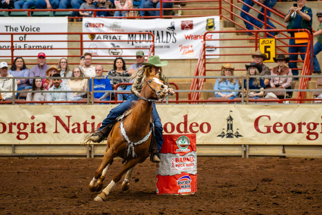 Barrel racer on a galloping horse turning around a barrel in an arena