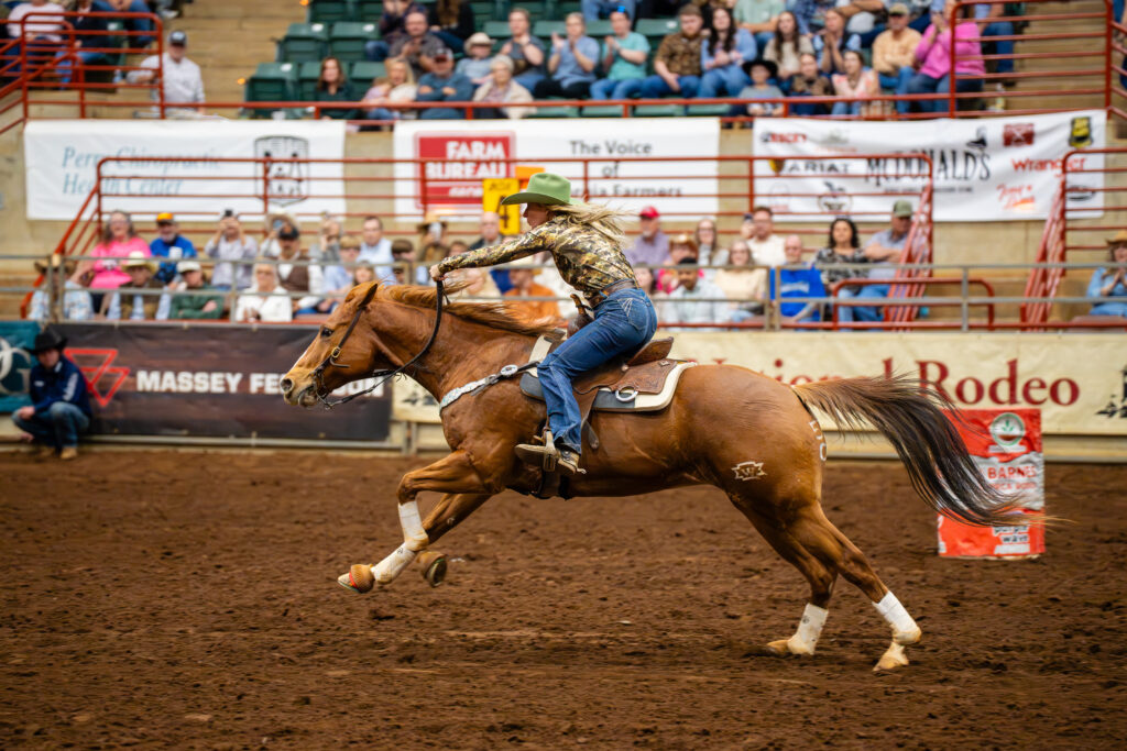 Barrel racer on galloping horse rounding a barrel in indoor arena