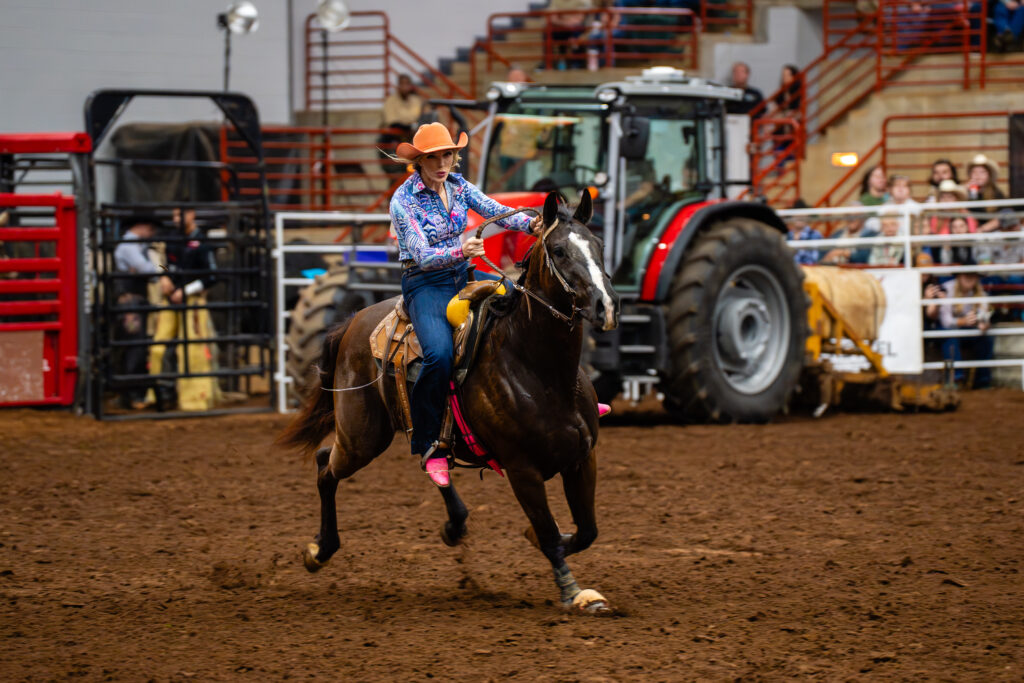 Cowgirl riding a galloping horse in a barrel racing rodeo arena
