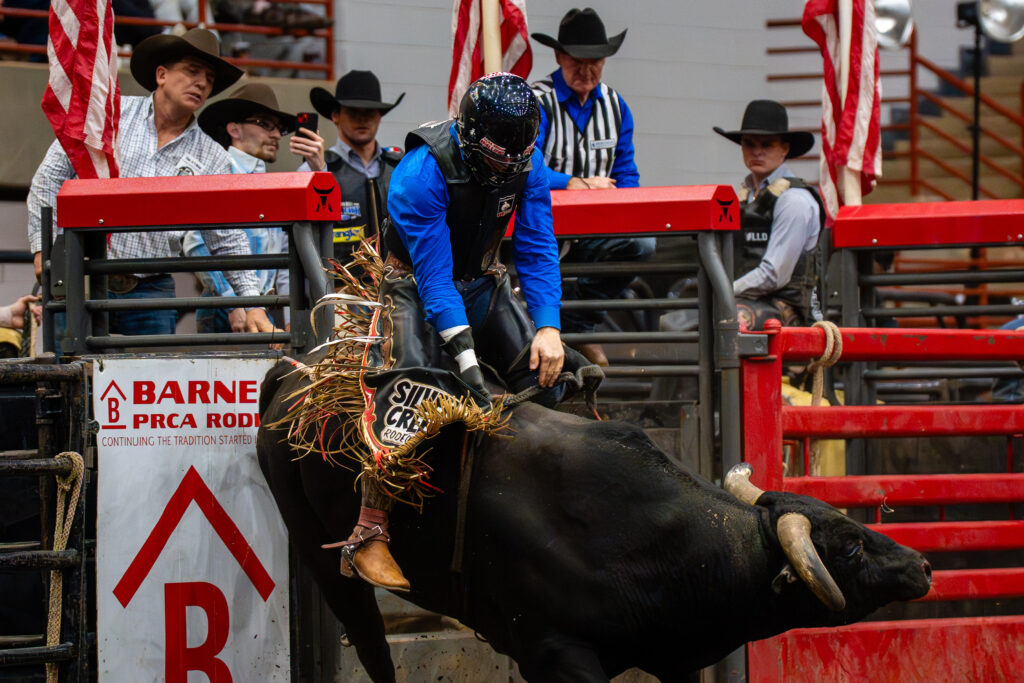 Bull rider in blue vest holding on during intense PRCA rodeo ride