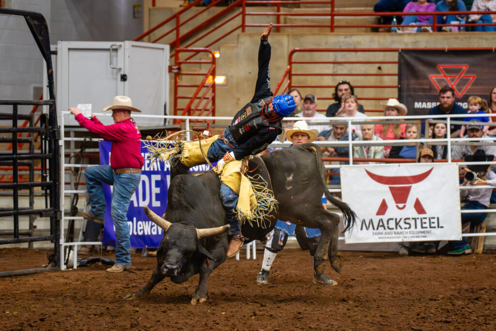 Bull rider in protective gear tries to stay mounted at an indoor rodeo