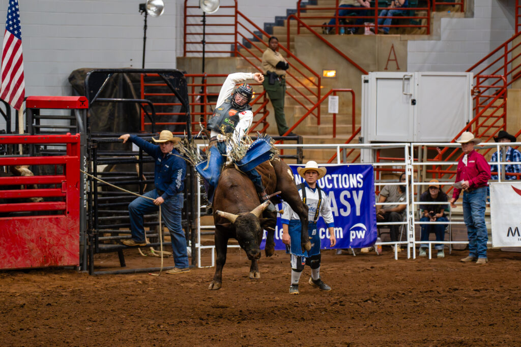 Bull rider holding on during a ride in an indoor rodeo arena