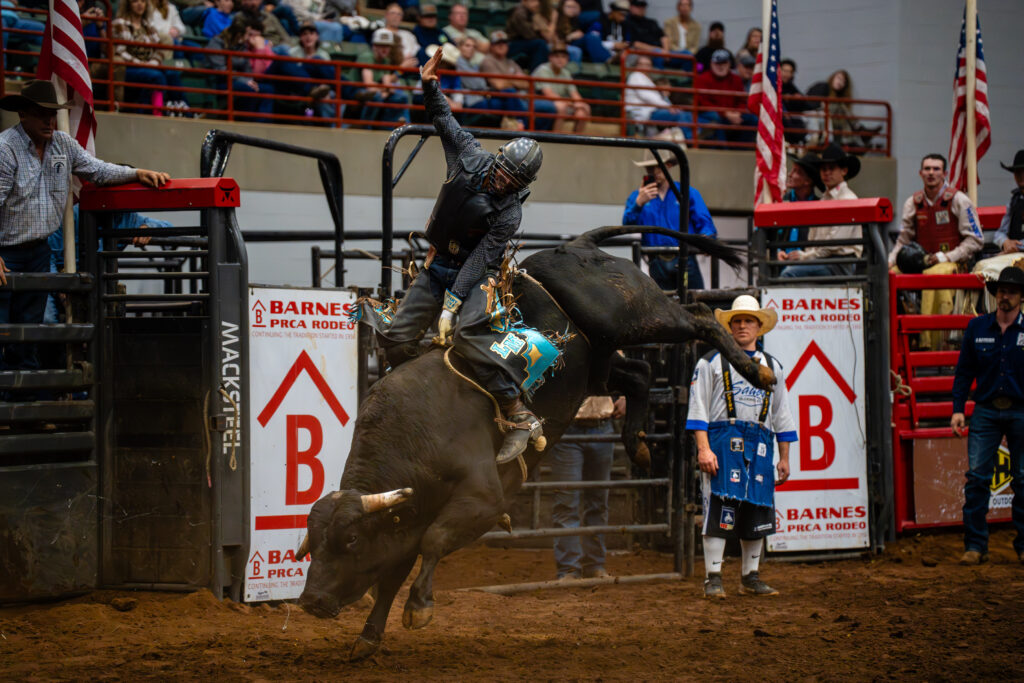 Bull rider holds on with one arm raised during a rodeo event