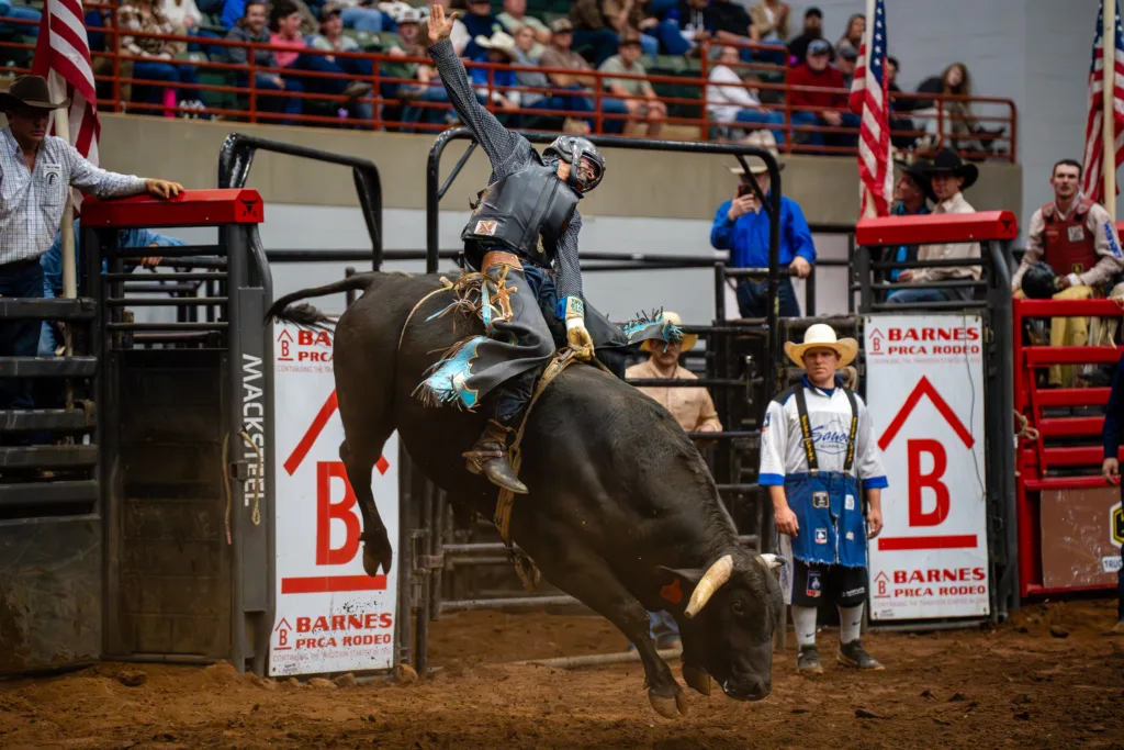 Bull rider balances on a bucking bull in an indoor rodeo arena