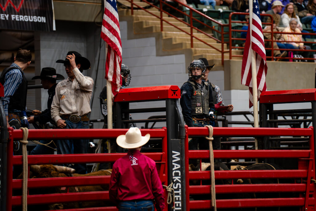 Bull riders and rodeo staff preparing in red chutes with flags