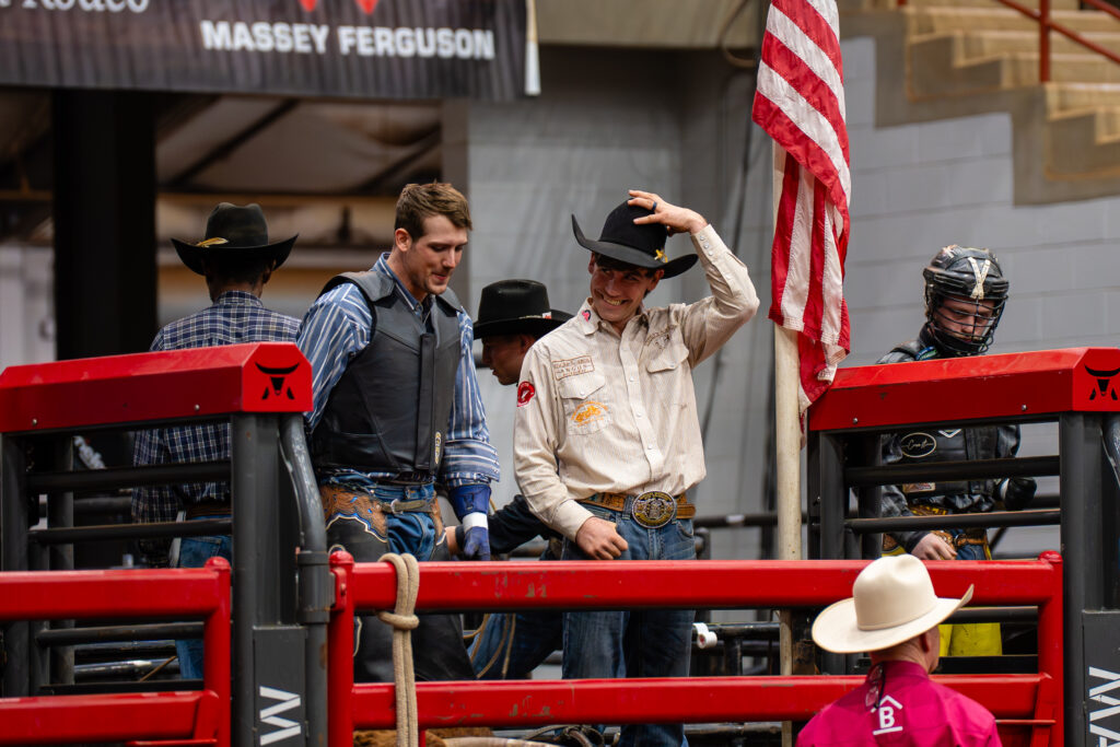 Cowboys in hats and vests stand by bull riding chute at rodeo
