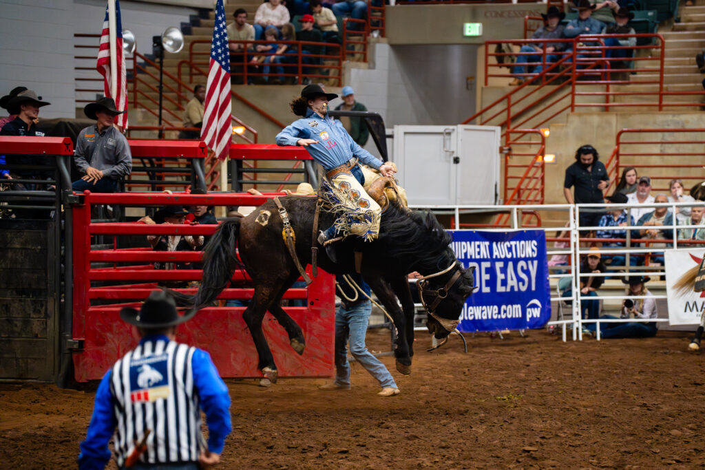 Cowboy riding a bucking horse in a saddle bronc event at an indoor rodeo