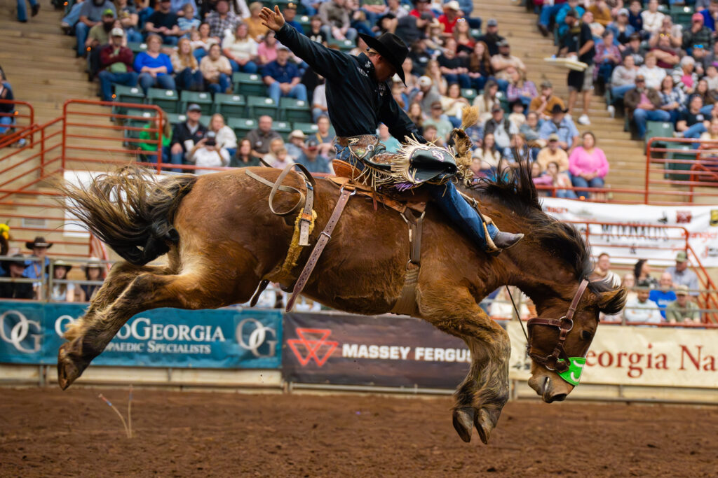 Cowboy riding a bucking bronc in an indoor rodeo arena