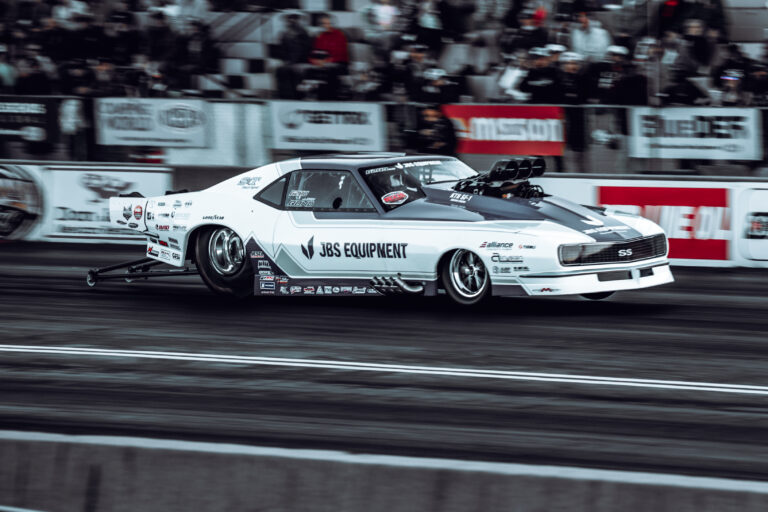 White drag racing car on the track in front of spectators at NHRA Saturday.